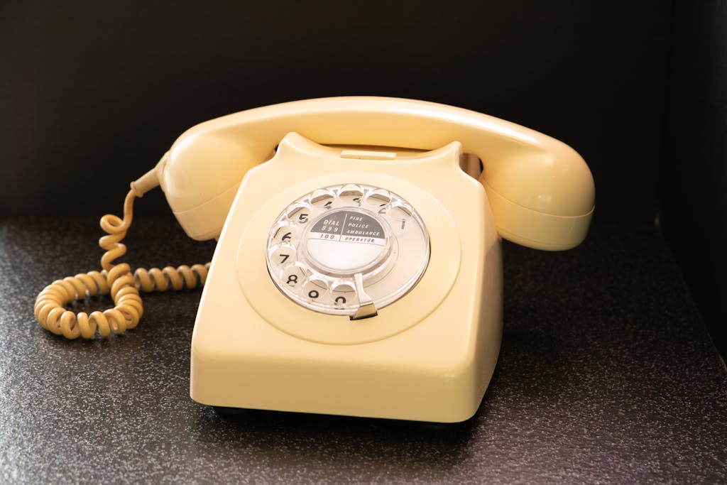 A vintage cream rotary dial telephone on a textured surface, showcasing retro technology.